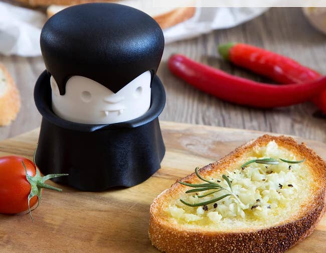 A garlic presser made to look like a vampire next to a piece of garlic bread
