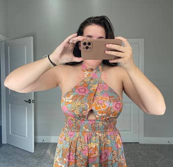 Person successful floral-patterned halter formal taking a reflector selfie indoors