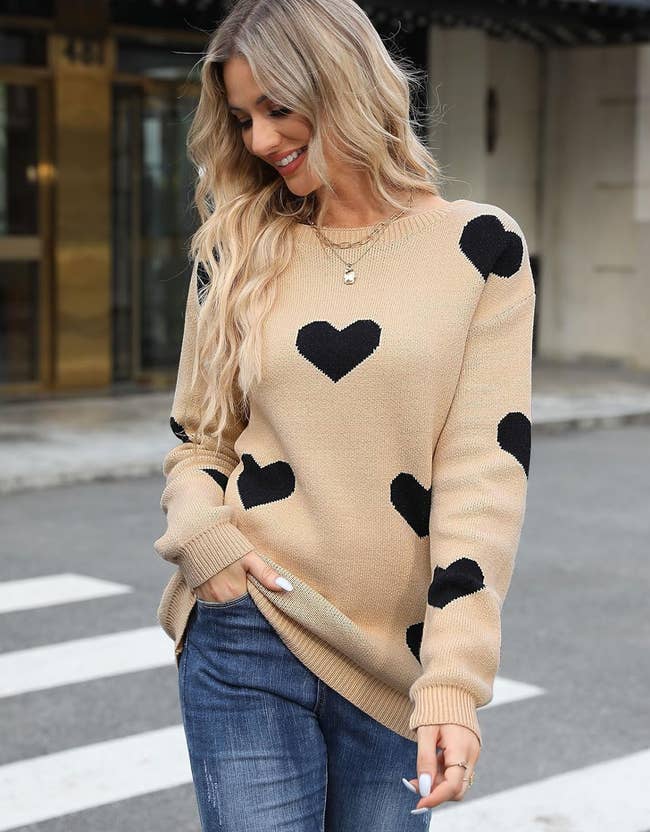 model wearing a tan sweater with black hearts on it