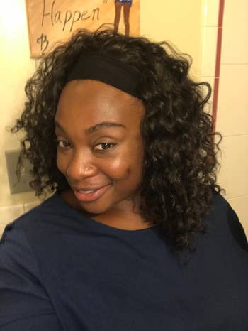 Person smiling, wearing a dark top and curly hairstyle with a headband