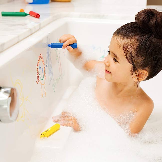 a child drawing with crayons in the tub