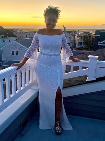Reviewer wearing off the shoulder lace maxi dress with side slit, diamond belt, and bell sleeves standing on white balcony with silver sandals