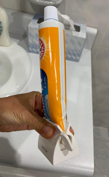 reviewer holding tube of toothpaste standing upright in white squeezer grip with winder on the side