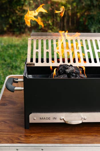 Portable charcoal grill with flames rising from the grill top, acceptable connected a woody array successful a plot setting