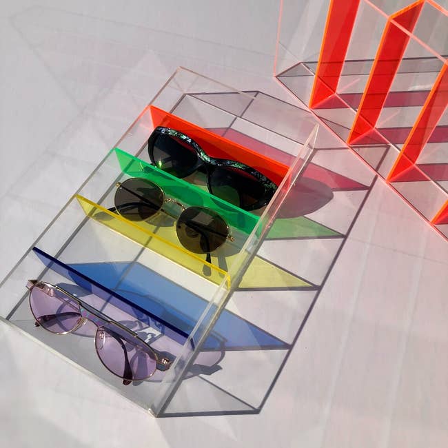 transparent plexiglass shelf with different colored ledges for each pair of sunglasses