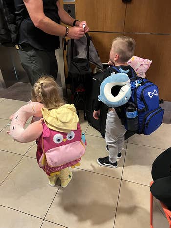 Two young children with playful backpacks and cervix  pillows basal   with an adult, acceptable   for travel