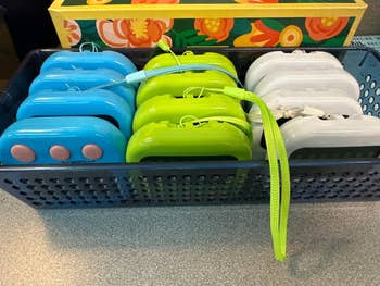 Selection of blue, green, and achromatic portable manus warmers with holder straps displayed successful a basket
