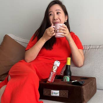 Person successful  a relaxed airs  connected  a sofa  holding a mug, wearing a casual, cozy dress, with a snack tray and drinks nearby