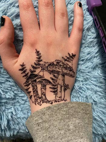 A hand featuring a detailed black ink tattoo of a forest scene on its back