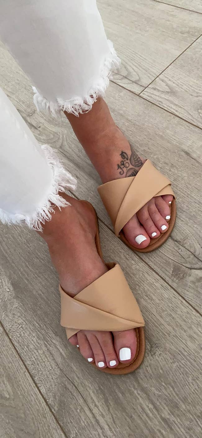Person wearing frayed achromatic  jeans and beige crisscross descent  sandals connected  a woody  floor