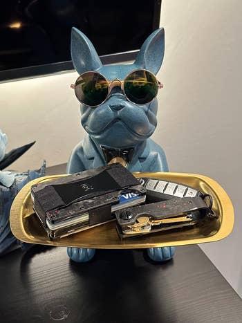 Sculpture of a dog with sunglasses holding a tray with a wallet and keys