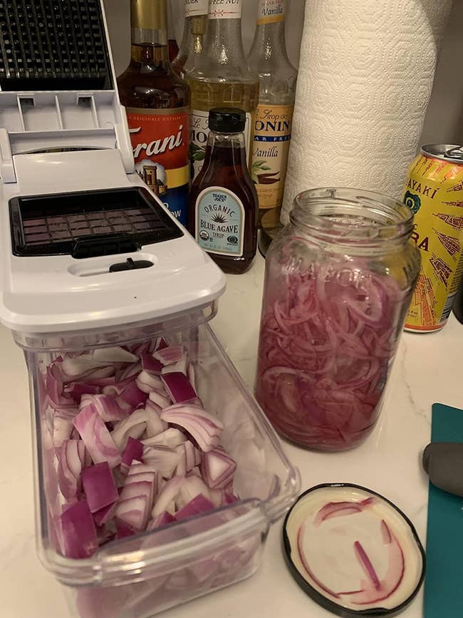 A kitchen counter with a jar of chopped pickled red onions, a chopping device with chopped onions