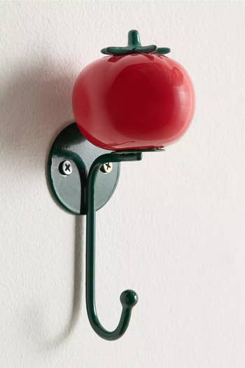 Wall hook shaped like a tomato with green stem detail, attached to a white wall. Ideal for kitchen or playful decor