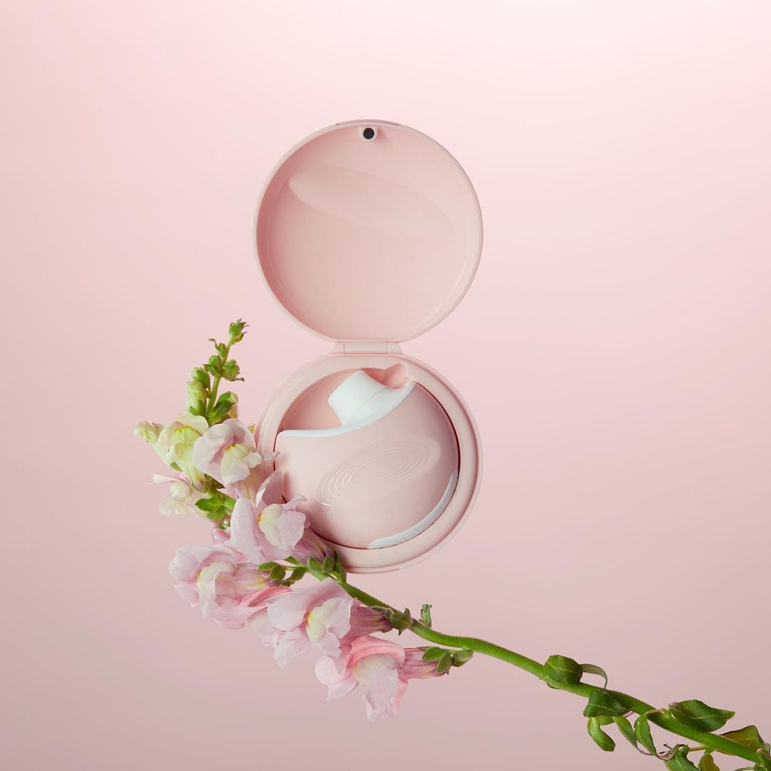 Pink suction vibrator in pink carrying case next to flower