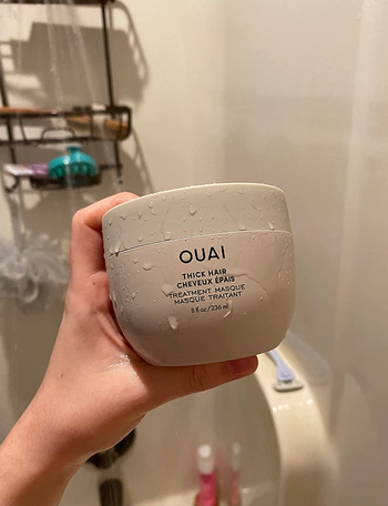 Reviewer holding jar of hair mask in the shower