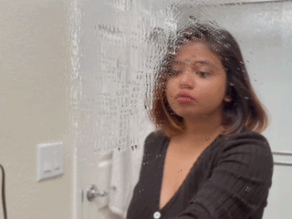 Person in a black top cleaning a bathroom mirror, using a squeegee