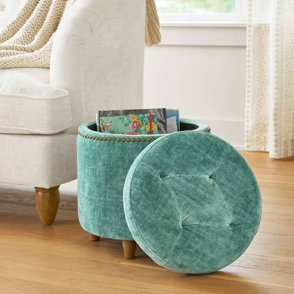 Round ottoman with lid off, revealing retention abstraction inside, adjacent to a sofa. Magazine disposable inside