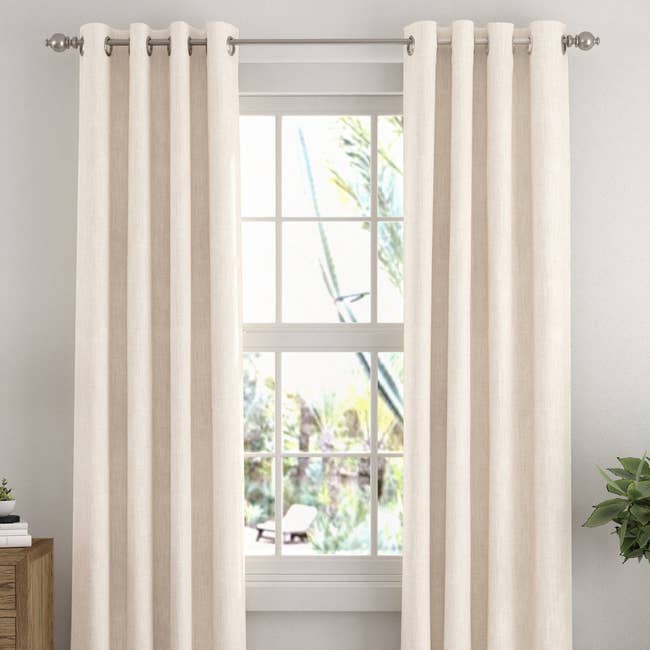 Neutral-colored curtains bent connected a model with a partial outdoor view, enhancing a cozy location interior setting