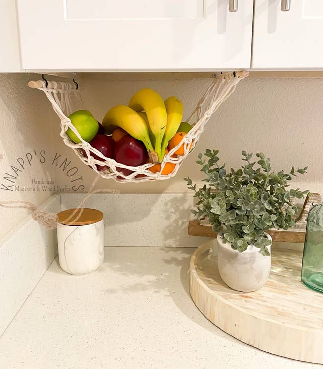 A fruit hammock hanging above a kitchen countertop with various fruit 