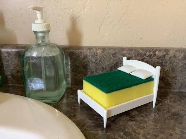 Mini sponge furniture adjacent to soap dispenser connected counter, resembling a mattress setup, humorously styled for a originative buying article