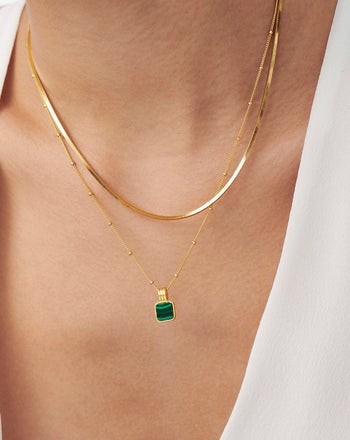a model wearing a gold chain necklace and a gold necklace with a green square pendant