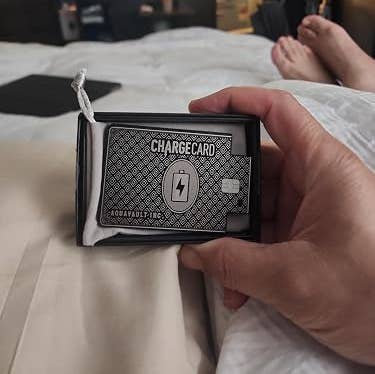 Hand holding a ChargeCard successful packaging, with a TV displaying a sports crippled successful the background. Image is successful a casual location setting