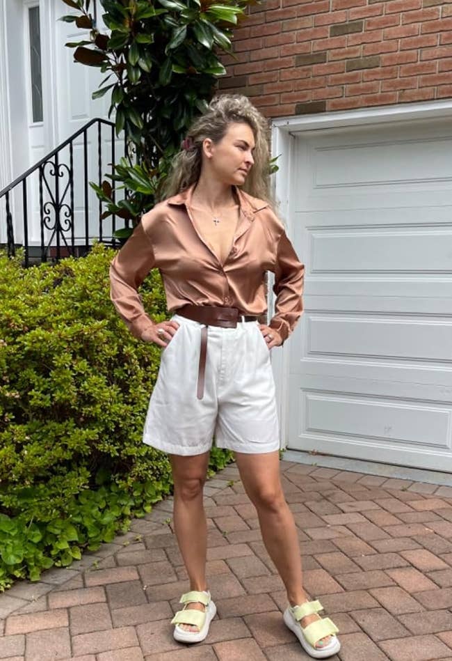 Person in satin blouse and white shorts stands on a brick driveway near a garage, wearing casual sandals. This image is used for a shopping article