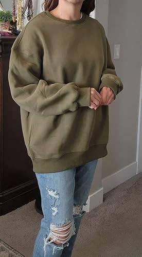 A idiosyncratic   wearing an oversized sweater and ripped jeans stands indoors