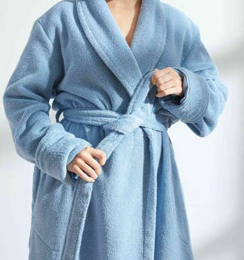 Person in a plush, belted bathrobe demonstrating its comfort and fit. The article discusses shopping for cozy, high-quality bathrobes