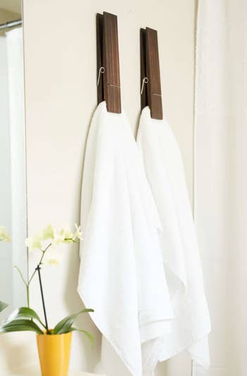 Two white towels hanging on wooden pegs in a bright bathroom, with a yellow potted plant to the side