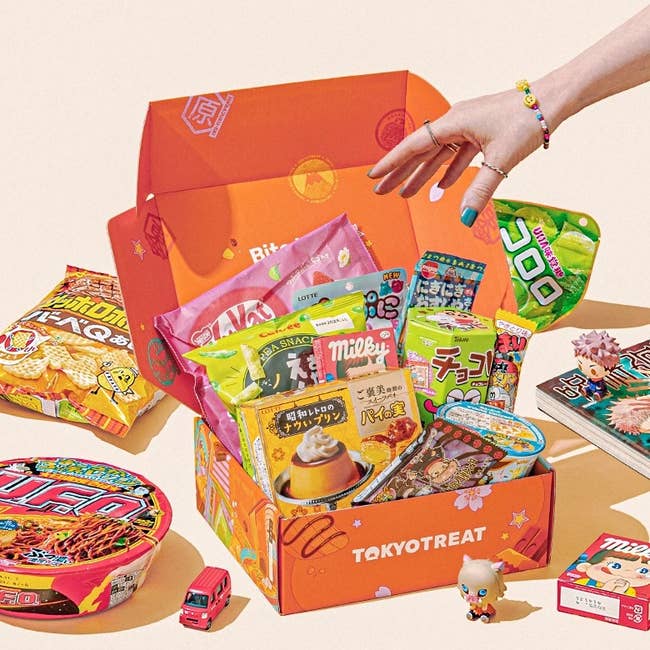 Variety of Japanese snacks and treats spilling retired of an unfastened TokyoTreat subscription box, with a manus reaching for an item
