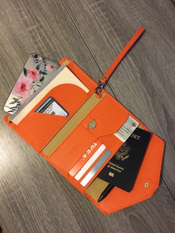 reviewer's orange travel wallet holding passport and other items