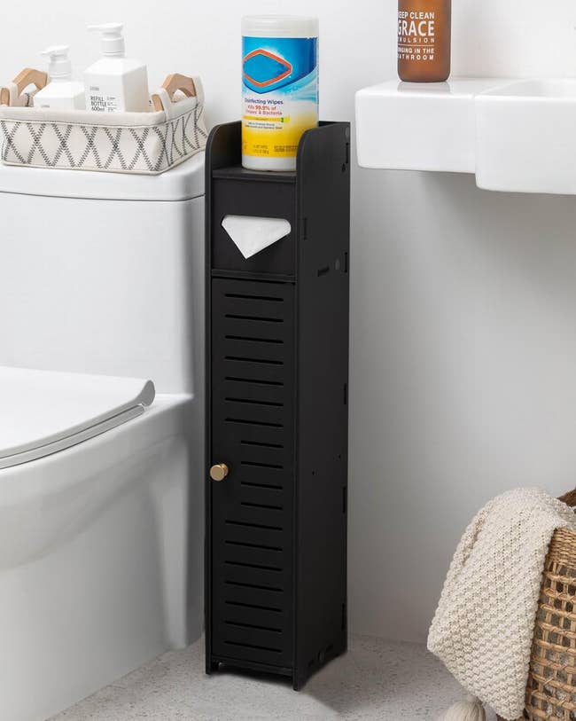 Slim black bathroom storage cabinet with a door, holding cleaning supplies and a paper towel under the sink. Accessible and space-efficient design