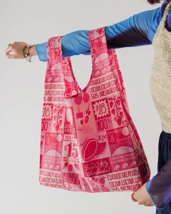 Person holding a bright patterned tote bag filled with groceries, visible against a plain background