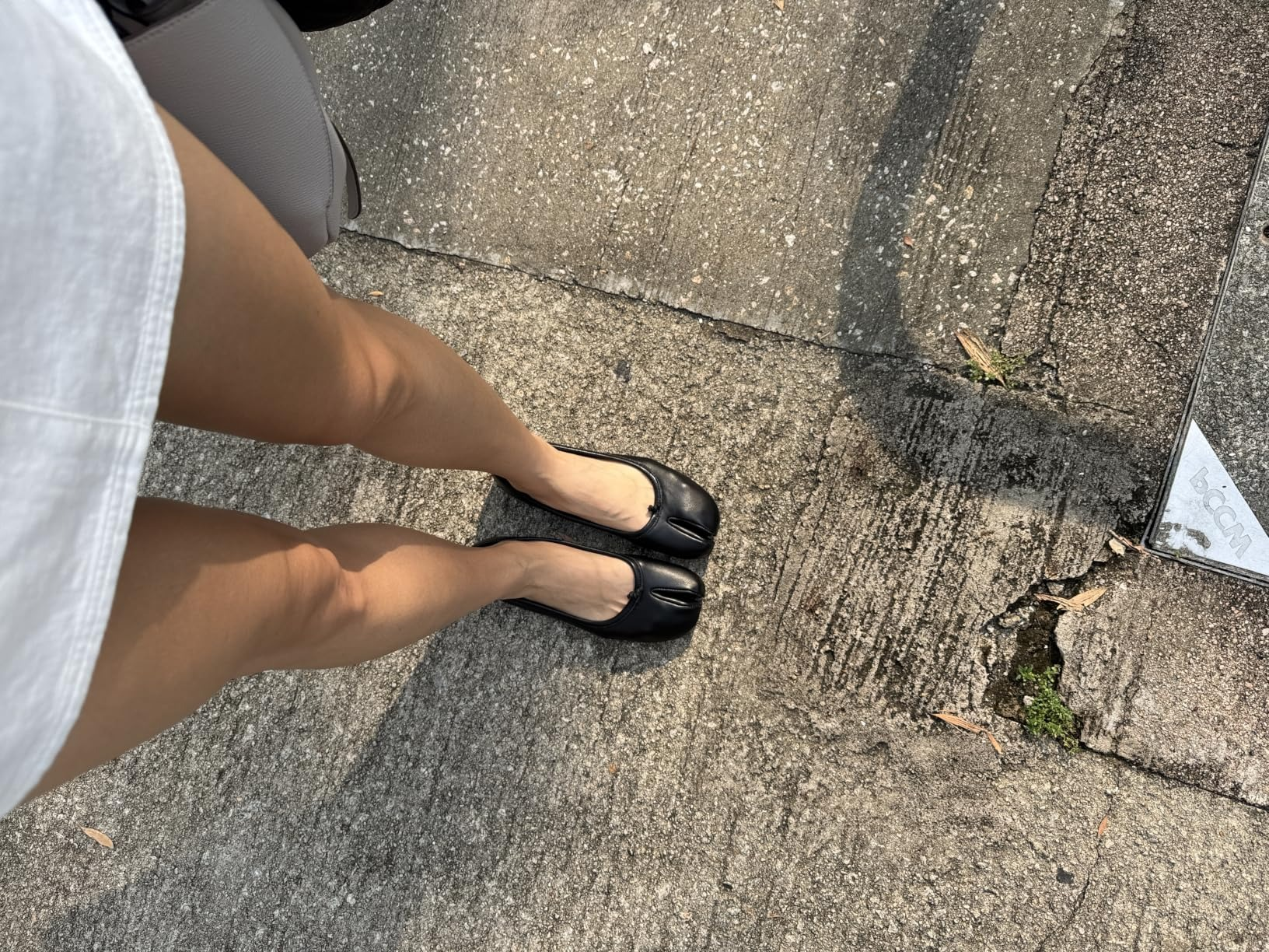 Person wearing achromatic  ballet flats and a achromatic  skirt stands connected  a textured pavement