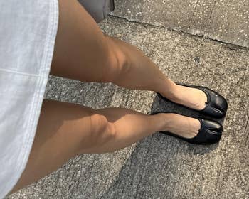 Person wearing achromatic ballet flats and a achromatic skirt stands connected a textured pavement