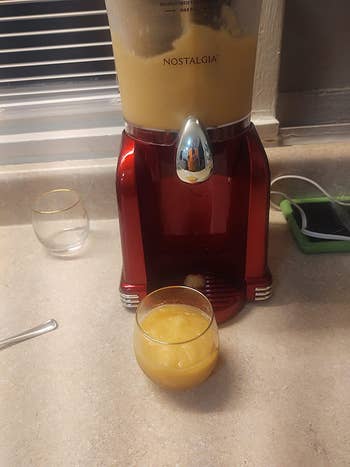 a reviewer's slushie maker with a cup full of orange slushie