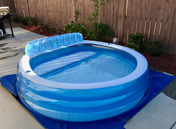 The round pool in a backyard with a builtin seat on one side of it 