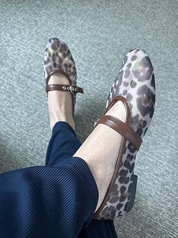 Person wearing leopard people     Mary Jane flats with brownish  straps and navy pants, sitting with 1  limb  crossed implicit    the other