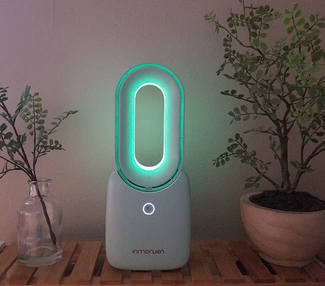 reviewer photo of the white fan on a side table, lit up with a soft green light