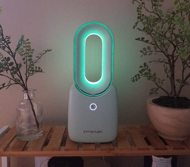 reviewer photo of the white fan on a side table, lit up with a soft green light