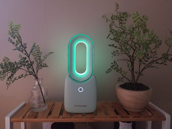reviewer photo of the white fan on a side table, lit up with a soft green light