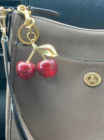 Close-up of a textured handbag with a cherry-shaped keychain attached to the handle
