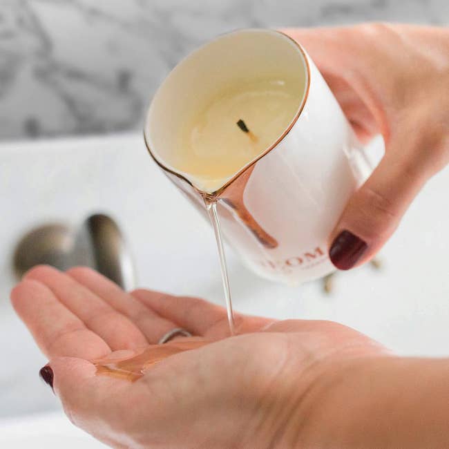 Hands pouring melted wax from a candle onto a palm, demonstrating skincare oregon relaxation merchandise use. Marble inheritance suggests a luxurious setting