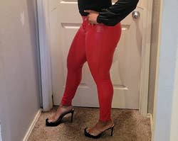 Reviewer showing side view of bright red faux leather pants with black heels and a black long sleeve top
