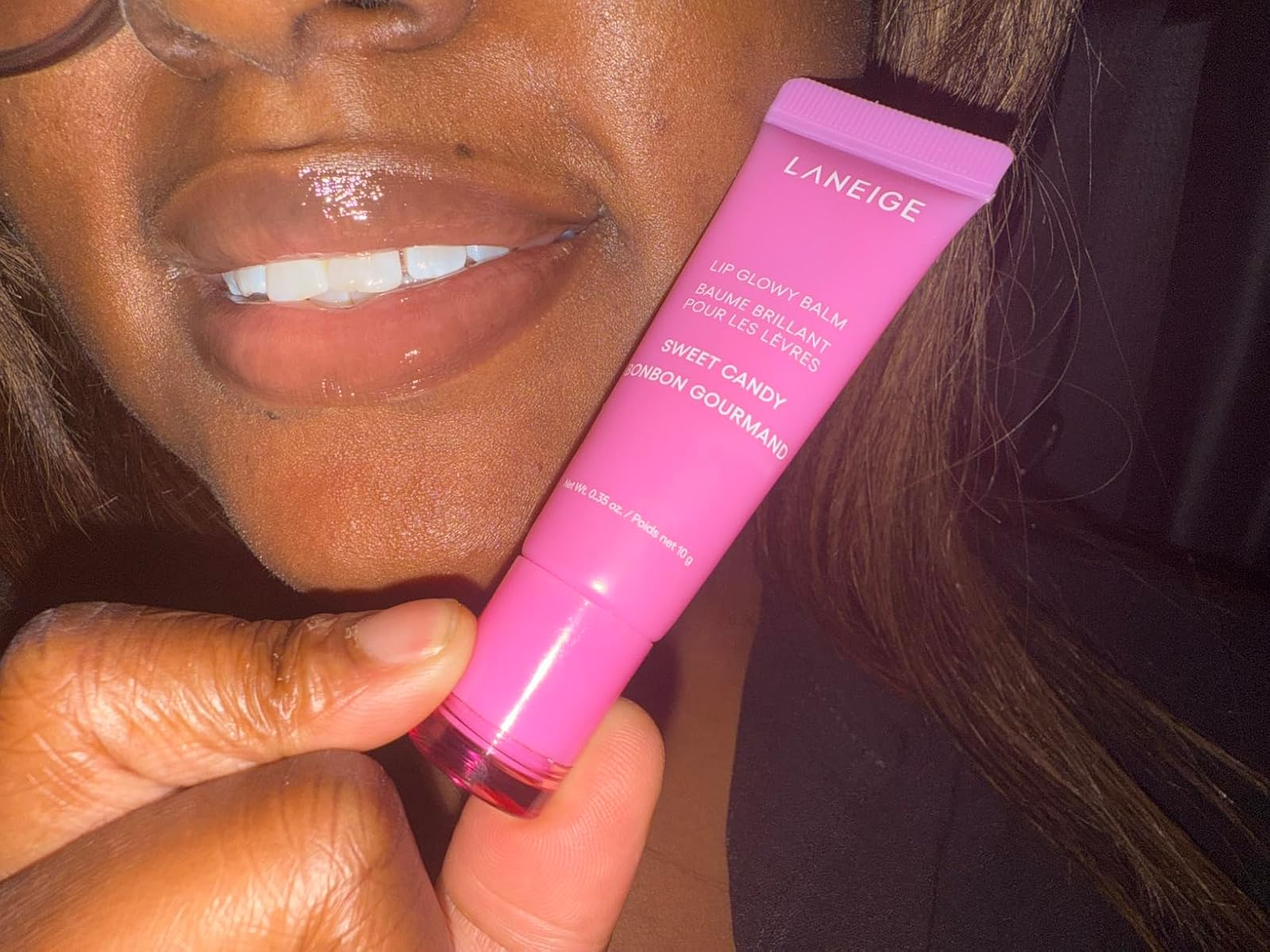 Person holding a conduit  of Laneige Lip Glowy Balm successful  Sweet Candy spirit  adjacent   their mouth, showcasing glossy lips