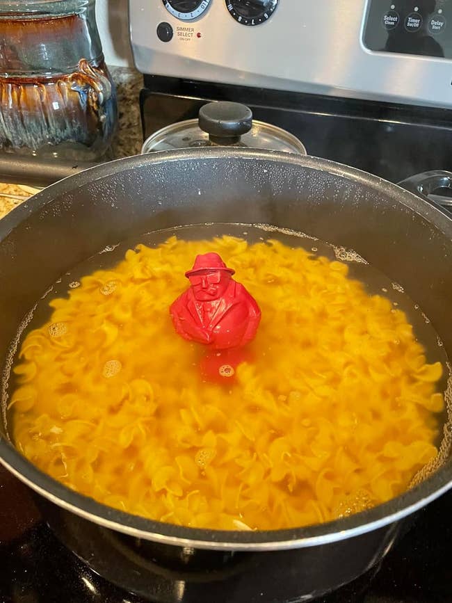 A novelty pasta measurer shaped like a person floats in a pot of boiling pasta