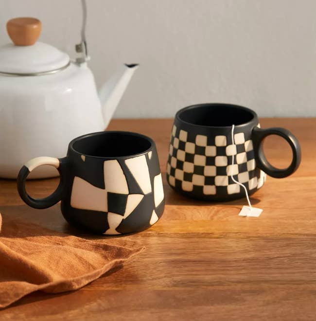 Two black and white matte mugs, one with abstract design and one with checkers 