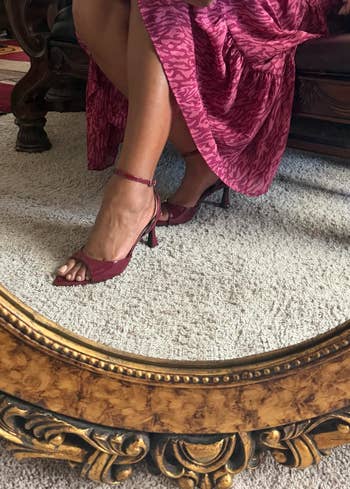 Woman seated, showing a red, patterned formal and open-toe heeled sandals, reflected successful a vintage-style mirror