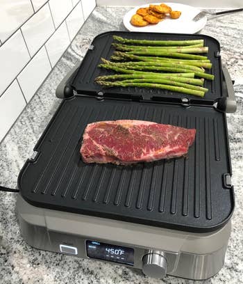 reviewer photo of the fully open griddler cooking a piece of steak and some asparagus